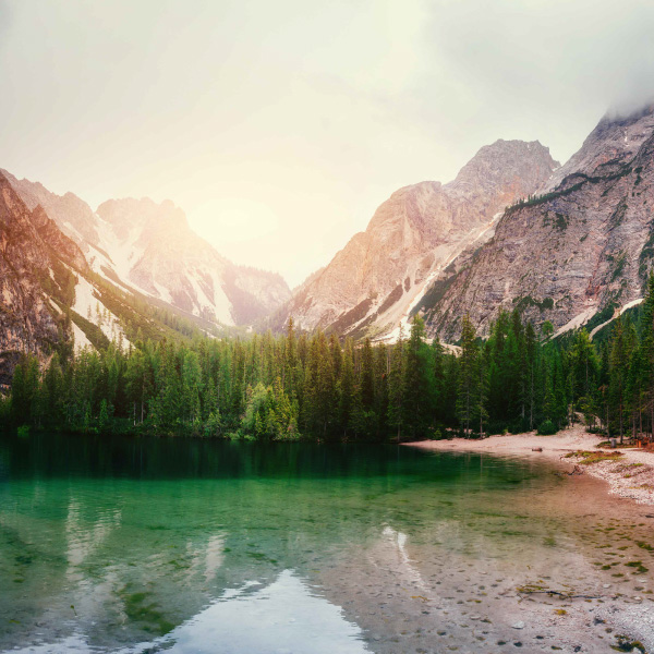 Green mountain lake with mountains and pink sky in the distance