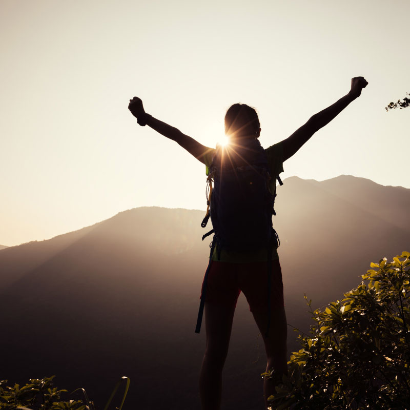 Silhouette of a hiker at top of a mountain with arms raised in celebration