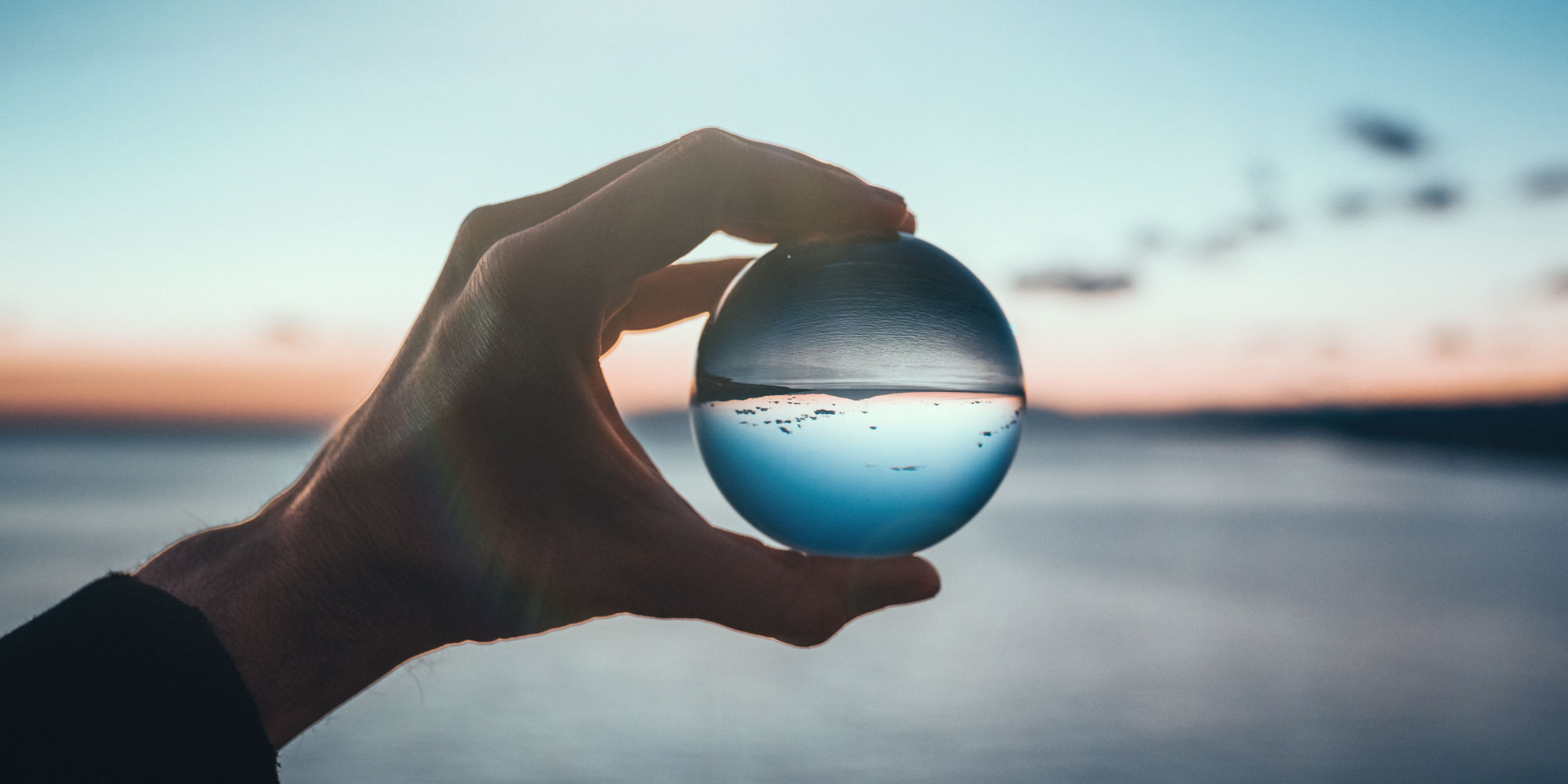 A hand holding a glass ball that inverts the horizon in the background